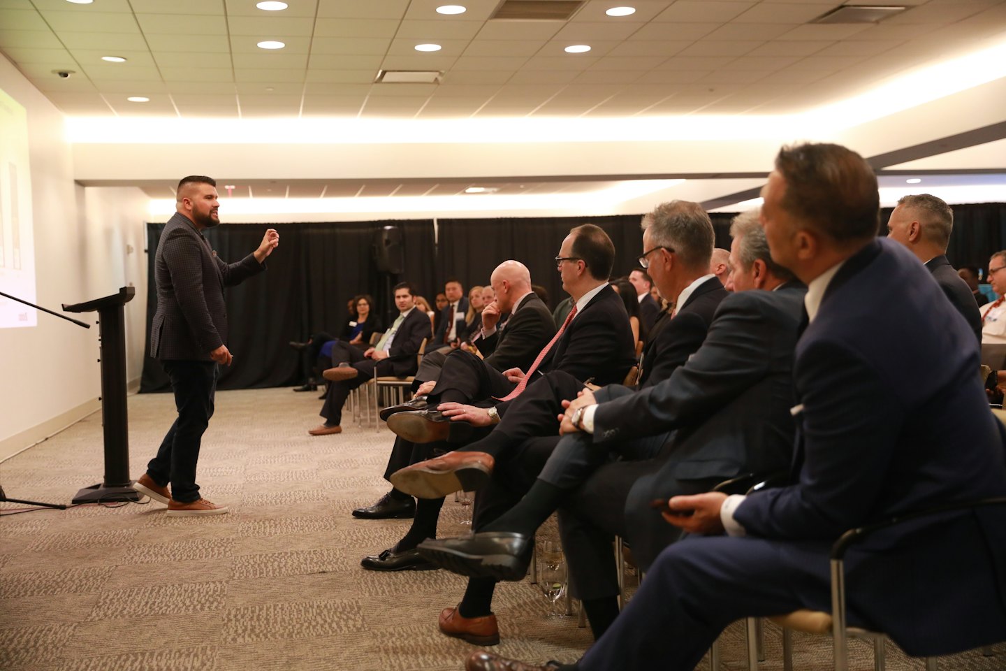 Man gestures while presenting a graph to an attentive business audience.